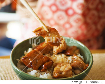 鶏モモ肉の照り焼き丼を食べている 107888602