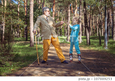 Grandfather walks with his granddaughter in the park. 107889253