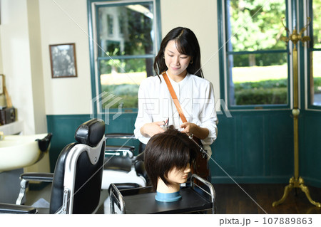 ヘアマネキンでカット練習をする女性美容師 ヘアマネキンでカット練習をする女性美容師 107889863