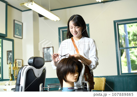 ヘアマネキンでカット練習をする女性美容師 ヘアマネキンでカット練習をする女性美容師 107889865