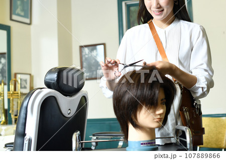 ヘアマネキンでカット練習をする女性美容師 ヘアマネキンでカット練習をする女性美容師 107889866