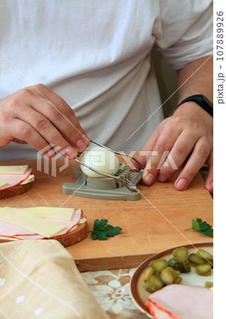 Cook's hand cutts boiled egg with egg cutter 107889926