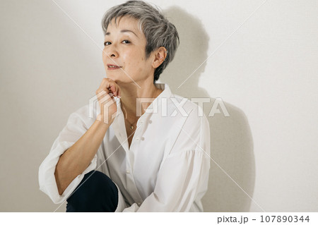 立膝で座る、白いシャツを着たグレイヘアの上品な日本人女性 立膝で座る、白いシャツを着たグレイヘアの上品な日本人女性 107890344