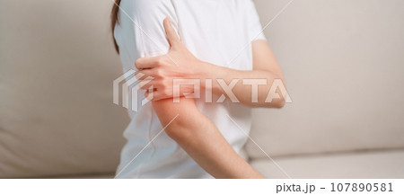 Woman having arm pain during sitting on couch at home, muscle injury and ache. Health and medical concept Woman having arm pain during sitting on couch at home, muscle injury and ache. Health and medical concept 107890581