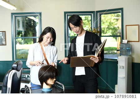 ヘアマネキンでカット練習する男女の美容師 ヘアマネキンでカット練習する男女の美容師 107891081