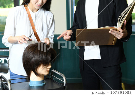ヘアマネキンでカット練習する男女の美容師 107891082