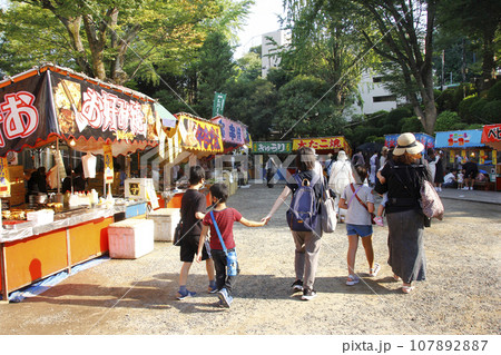 縁日の露店の写真。親子で連れ立って縁日を散策して目的の露店を探す。其々の好きな食べ物を食べながら歩く 縁日の露店の写真。親子で連れ立って縁日を散策して目的の露店を探す。其々の好きな食べ物を食べながら歩く 107892887