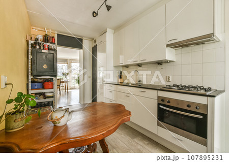a kitchen with white cabinets and wood table in the middle of the room, there is an oven on the wall a kitchen with white cabinets and wood table in the middle of the room, there is an oven on the wall 107895231