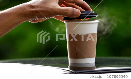 coffee takeaway in a paper cup on top of the car roof green tree background at sunrise in the morning, selective focus, soft focus. coffee takeaway in a paper cup on top of the car roof green tree background at sunrise in the morning, selective focus, soft focus. 107896340