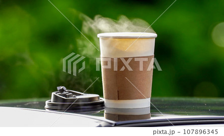 coffee takeaway in a paper cup on top of the car roof green tree background at sunrise in the morning, selective focus, soft focus. coffee takeaway in a paper cup on top of the car roof green tree background at sunrise in the morning, selective focus, soft focus. 107896345