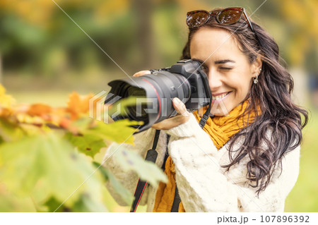 A smiling female photographer takes pictures of autumn leaves with her professional camera. A smiling female photographer takes pictures of autumn leaves with her professional camera. 107896392