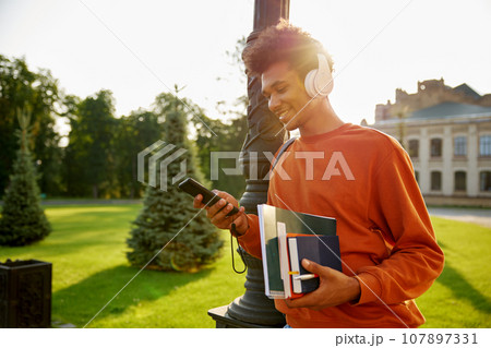 Side view portrait of happy smiling teenager student in headset using phone 107897331