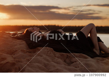 Woman relaxing on beach at sunset 107900992