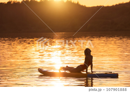 Beautiful woman practicing yoga on paddle sup surfboard. Beautiful woman practicing yoga on paddle sup surfboard. 107901888
