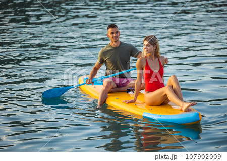 Woman and man surfing in ocean on sup board ar summer vacation. 107902009