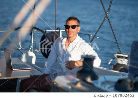 Contented man in sunglasses sitting on a yacht deck with a cup of coffee Contented man in sunglasses sitting on a yacht deck with a cup of coffee 107902452