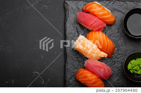Traditional Japanese sushi with soy sauce, wasabi, chopsticks top view on dark black rustic slate. Sushi with salmon, tuna, shrimp, space for text Traditional Japanese sushi with soy sauce, wasabi, chopsticks top view on dark black rustic slate. Sushi with salmon, tuna, shrimp, space for text 107904480