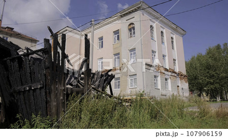 View of an old abandoned house with fallen plaster. Clip. Green grass and old burnt wooden building. View of an old abandoned house with fallen plaster. Clip. Green grass and old burnt wooden building. 107906159