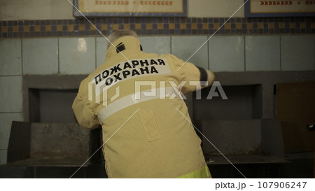 Rear view of a fireman getting ready for the call. Clip. Man getting dressed in protective jacket. 107906247