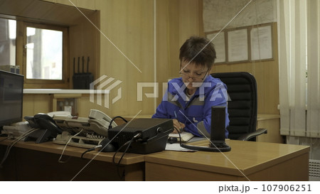 Woman in blue uniform working at the table. Clip. Emergency worker doing administrative work and writing. Woman in blue uniform working at the table. Clip. Emergency worker doing administrative work and writing. 107906251