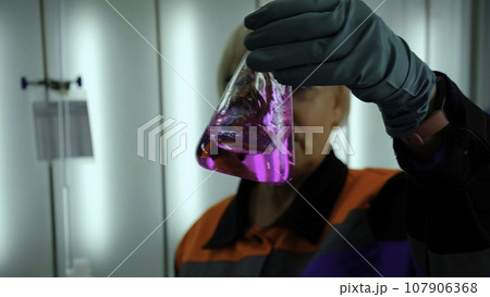 Chemist holds flask with pink liquid, shakes it and fluid substance changes color. Clip. Pink mixture becoming transparent. 107906368