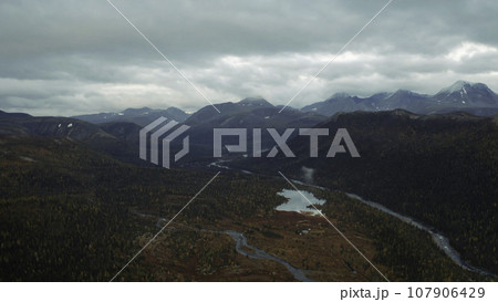 Aerial flight over amazing small lake surrounded by forested valley and mountains. Clip. Untouched nature from above on late autumn day. 107906429