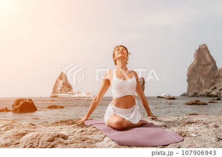 Fitness woman sea. A happy middle aged woman in white sportswear exercises morning outdoors on a beach with volcanic rocks by the sea. Female fitness pilates yoga routine concept. Healthy lifestyle. Fitness woman sea. A happy middle aged woman in white sportswear exercises morning outdoors on a beach with volcanic rocks by the sea. Female fitness pilates yoga routine concept. Healthy lifestyle. 107906943