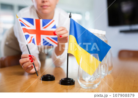 Unrecognizable girl sets midget Ukrainian and Britannic flags before international negotiations 107908879