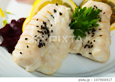 Codfish prepared on steam and served with greens and lemon 107908917