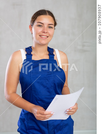 Young woman in work overalls posing with documents 107908937