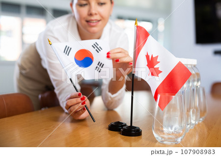 Young woman puts flags of South Korea and Canada on table in office 107908983