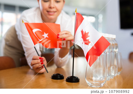 Young woman putting flags of Turkey and Canada on table in office 107908992