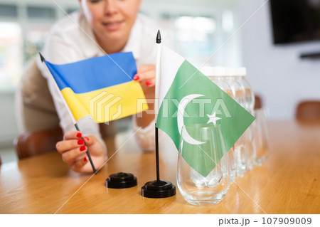 Young woman puts flags of Ukraine and Pakistan on table in office Young woman puts flags of Ukraine and Pakistan on table in office 107909009