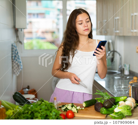 Woman using phone while making vegetable salad 107909064