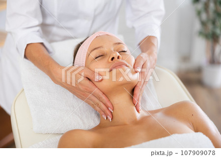 Young female client receiving soothing and relaxing facial massage 107909078
