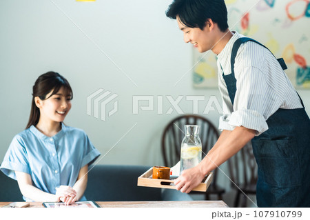 カフェでブランチを取る若い女性とエプロン姿の店員 107910799