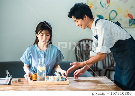 カフェでブランチを取る若い女性とエプロン姿の店員 カフェでブランチを取る若い女性とエプロン姿の店員 107910800