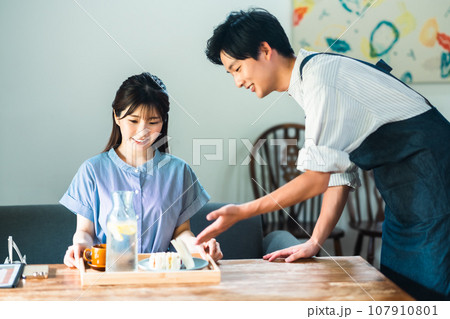 カフェでブランチを取る若い女性とエプロン姿の店員 カフェでブランチを取る若い女性とエプロン姿の店員 107910801