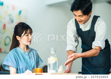 カフェでブランチを取る若い女性とエプロン姿の店員 カフェでブランチを取る若い女性とエプロン姿の店員 107910804