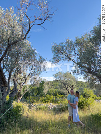Smiling man and woman standing near green tree in garden Smiling man and woman standing near green tree in garden 107913577