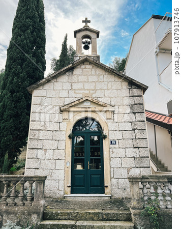 Bell with a cross over an old stone chapel with a green wooden door 107913746