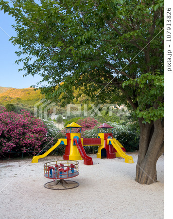 Colorful slides with transitions in the form of a castle next to the carousel stand on a playground in a green park Colorful slides with transitions in the form of a castle next to the carousel stand on a playground in a green park 107913826
