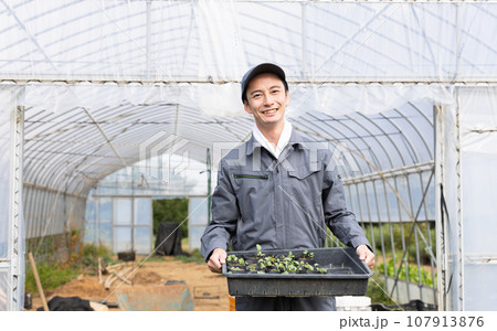 ビニールハウスの前に立つ農家の男性 107913876