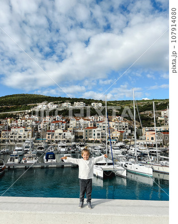 Little girl stands on the pier against the backdrop of moored yachts Little girl stands on the pier against the backdrop of moored yachts 107914080