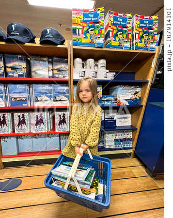 Little girl with a basket of books stands in a bookstore Little girl with a basket of books stands in a bookstore 107914101