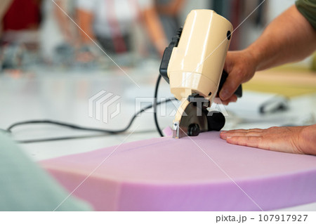 Hands of a furniture master cut a piece of foam with foam cutting machine Hands of a furniture master cut a piece of foam with foam cutting machine 107917927