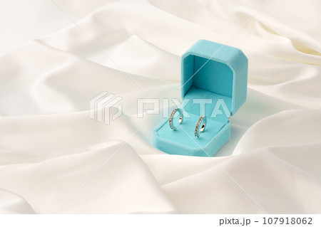 White gold earrings in blue jewelry box on silk background White gold earrings in blue jewelry box on silk background 107918062
