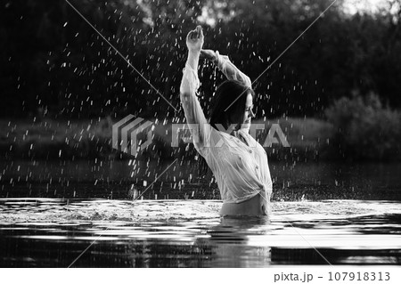 Happy blonde woman having fun in sunny park smiling, fooling around, laughing. Slow Motion. Beautiful caucasian girl dancing under the summer rain. wet hair and clothes. enjoying with drops. 107918313