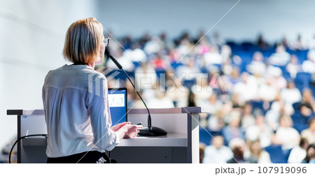 Female speaker giving a talk on corporate business conference. Unrecognizable people in audience at conference hall. Business and Entrepreneurship event Female speaker giving a talk on corporate business conference. Unrecognizable people in audience at conference hall. Business and Entrepreneurship event 107919096