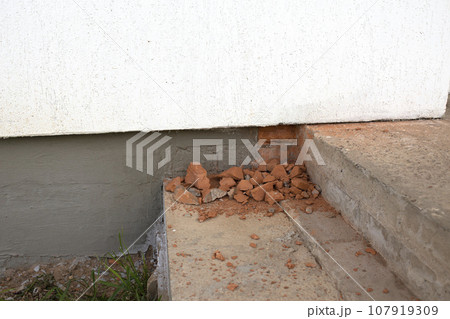 Broken red brick neatly lays on the steps near the foundation of the house. The concept of finishing a house outside. Broken red brick neatly lays on the steps near the foundation of the house. The concept of finishing a house outside. 107919309